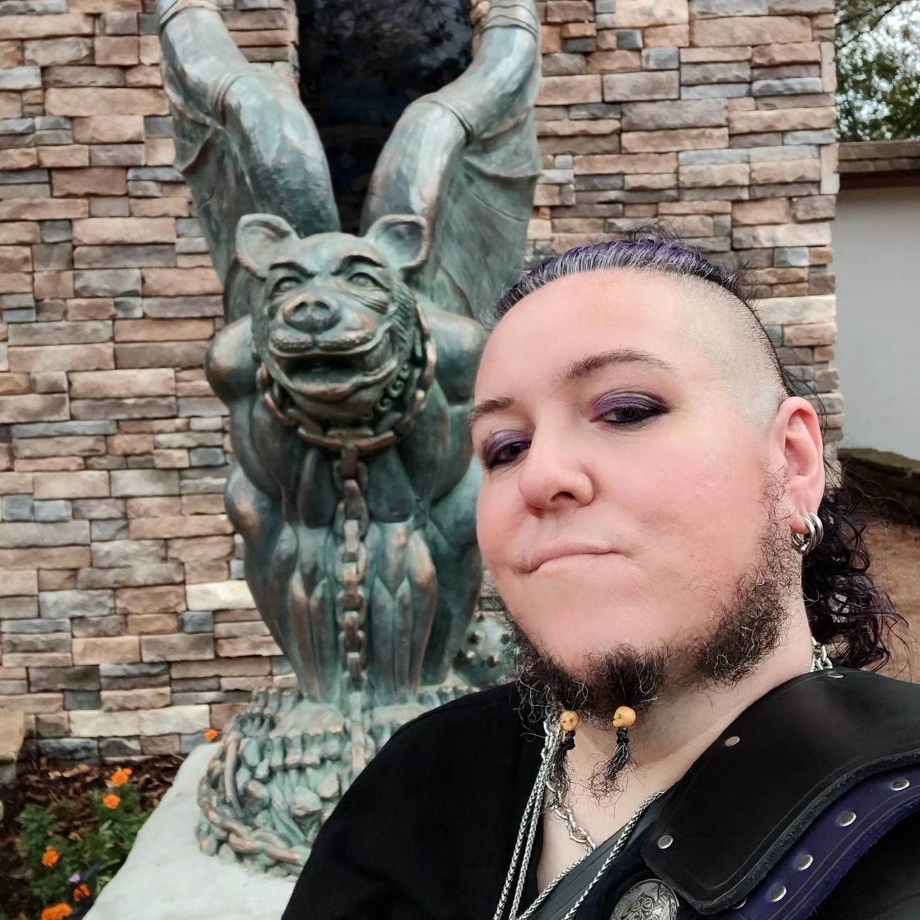 Photograph of the artist standing in front of a bronze gargoyle statue at the Texas Renaissance Faire